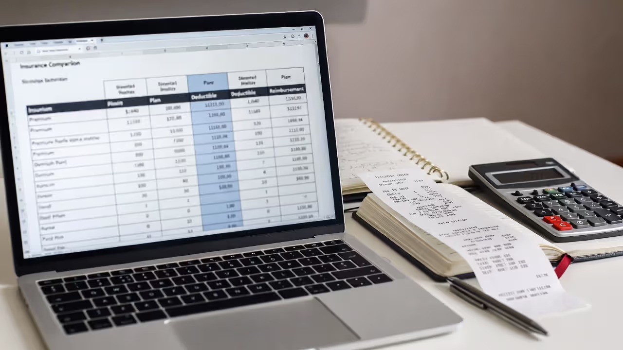 Desk with a laptop comparing pet insurance options, blurred vet receipts, and a calculator